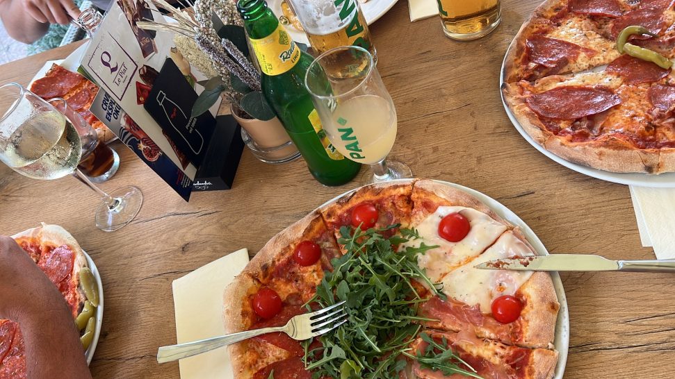 Letzter Abend Ein Tisch mit Pizzastücken, Rucola, Getränken und Speisekarten.